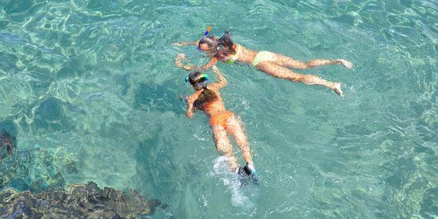 Dos chcias practicando esnórquel en una playa con aguas transparentes.